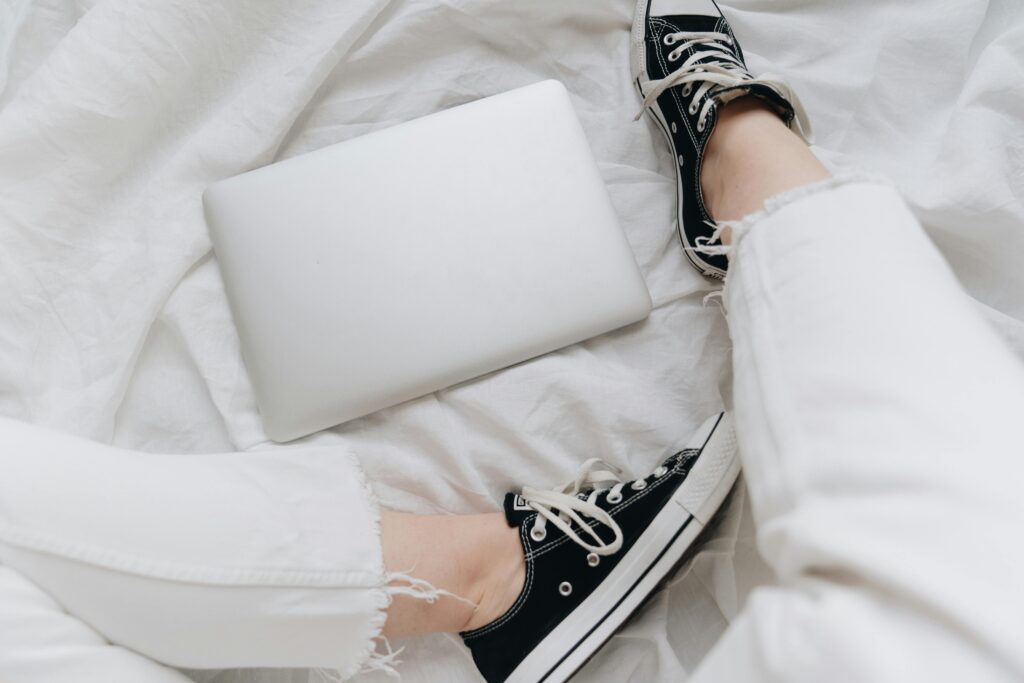 Top-down view of stylish black sneakers and a laptop on white linen, exuding a relaxed vibe.