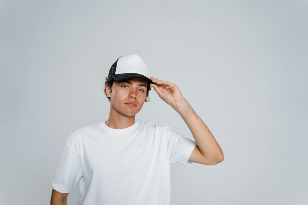 Portrait of a young man in a white shirt and a cap posing in a studio setting.